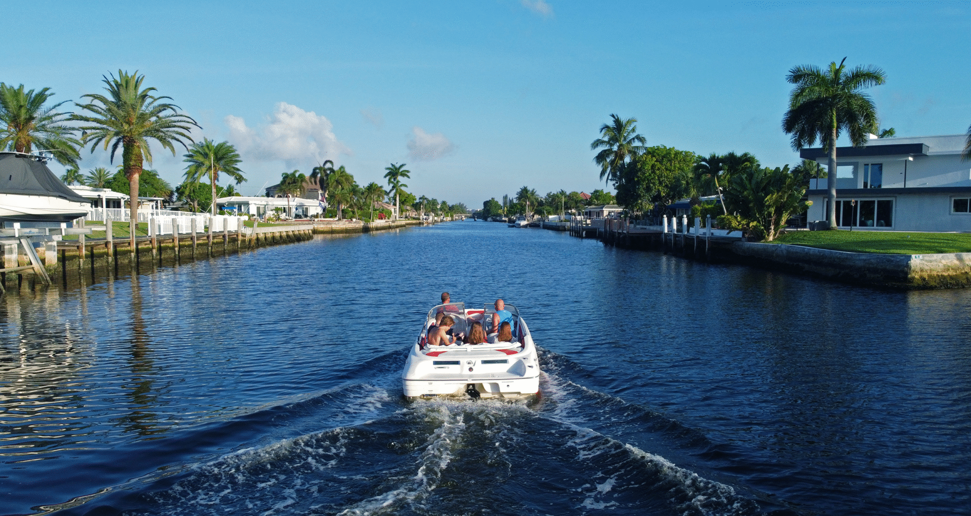 Ciudad turística soleada. Lancha navega por canal bordeado de palmeras y casas. Inversión inmobiliaria en destinos turísticos de México.