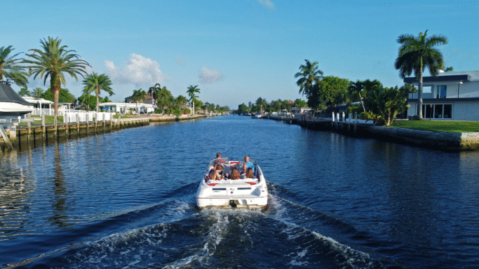 Ciudad turística soleada. Lancha navega por canal bordeado de palmeras y casas. Inversión inmobiliaria en destinos turísticos de México.