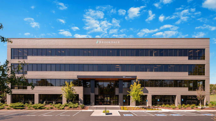 Fachada del edificio Brookdale, un proveedor líder en viviendas para mayores. Welltower invierte en su crecimiento. Cielo azul con nubes y estacionamiento.