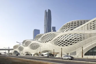 Diseño de estación de hidrógeno por Zaha Hadid Architects: estructura ondulada blanca con ventanas geométricas y rascacielos al fondo en un paisaje urbano.