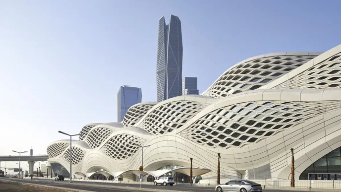 Diseño de estación de hidrógeno por Zaha Hadid Architects: estructura ondulada blanca con ventanas geométricas y rascacielos al fondo en un paisaje urbano.