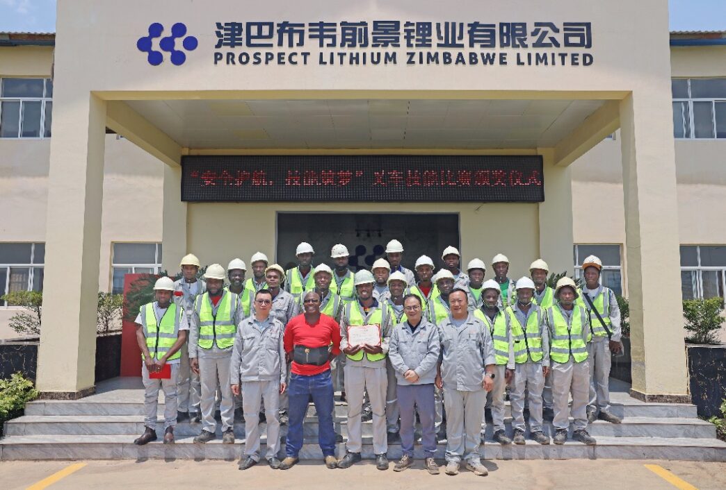 Grupo posando frente a Prospect Lithium Zimbabwe Limited, impulsando energía renovable en planta solar de 70MW. Celebración de éxito y compromiso.
