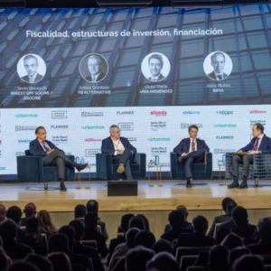 Panel de expertos discutiendo fiscalidad, inversión y financiación en evento Quienes Somos. Oradores y público presentes. Asuntos empresariales.