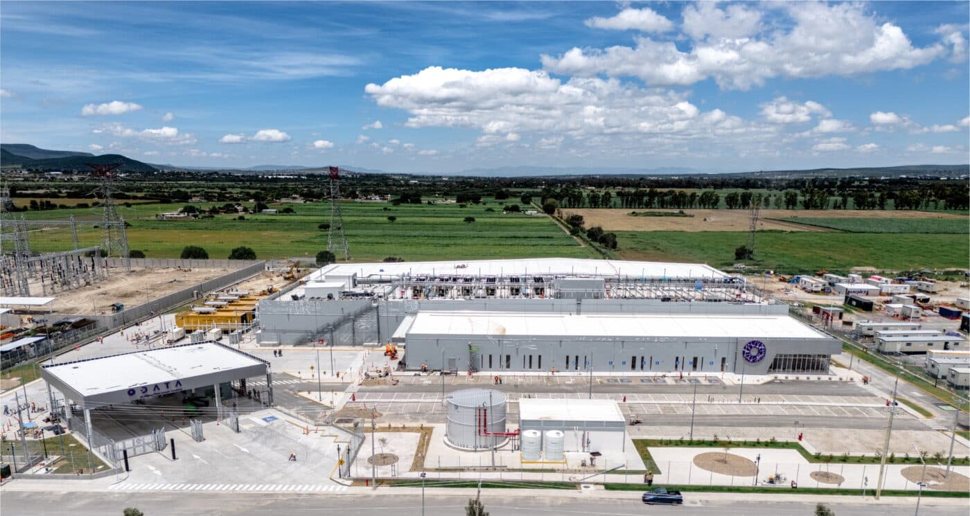Vista aérea de instalaciones industriales en Querétaro con edificios blancos, estacionamiento y áreas verdes bajo cielo azul.