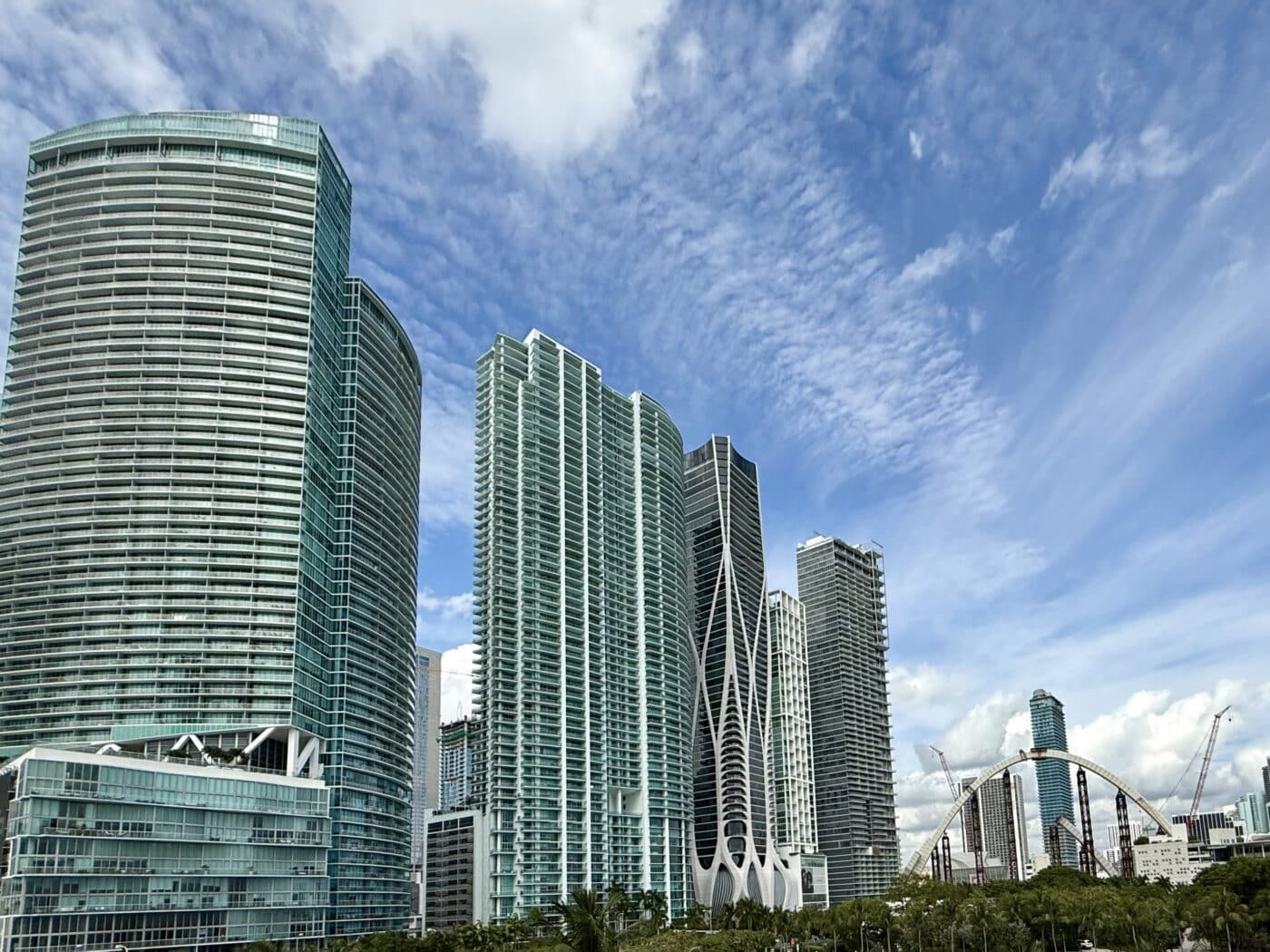 Persona frente a condominio alto de cristal azul bajo cielo parcialmente nublado en ciudad del sur de Florida.
