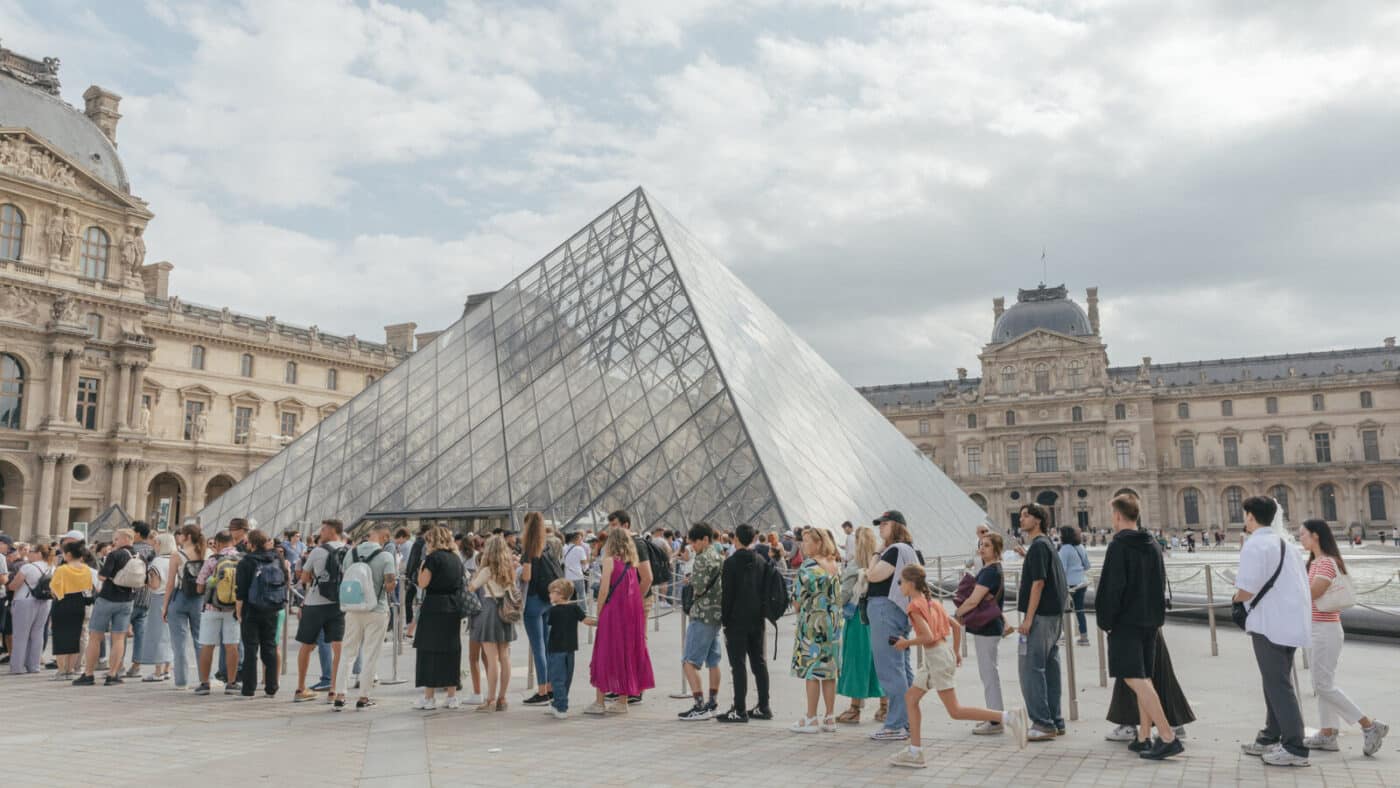 Gente frente a la Pirámide del Louvre, esperando para entrar. Renovación del Museo del Louvre en Francia. Fachada del Museo y cielo nublado.