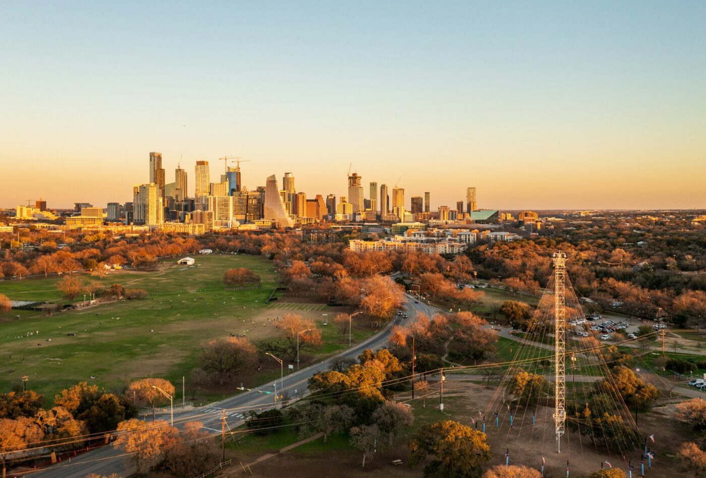 Vista aérea del skyline de Houston con parque, unidades habitacionales y persona bajo cables de alta tensión al atardecer.