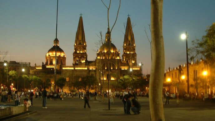 Vista nocturna de la Catedral de Guadalajara, México, con su arquitectura iluminada y gente paseando en la plaza. Destino turístico popular.