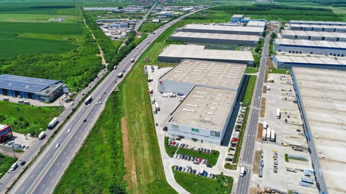 Vista aérea de un parque industrial con grandes almacenes, carretera transitada y zonas verdes. Edificios modernos y logística empresarial.