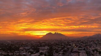 Amanecer en Monterrey, México, con el Cerro de la Silla destacando en el horizonte bajo un cielo naranja y nubes espectaculares. Vista panorámica.