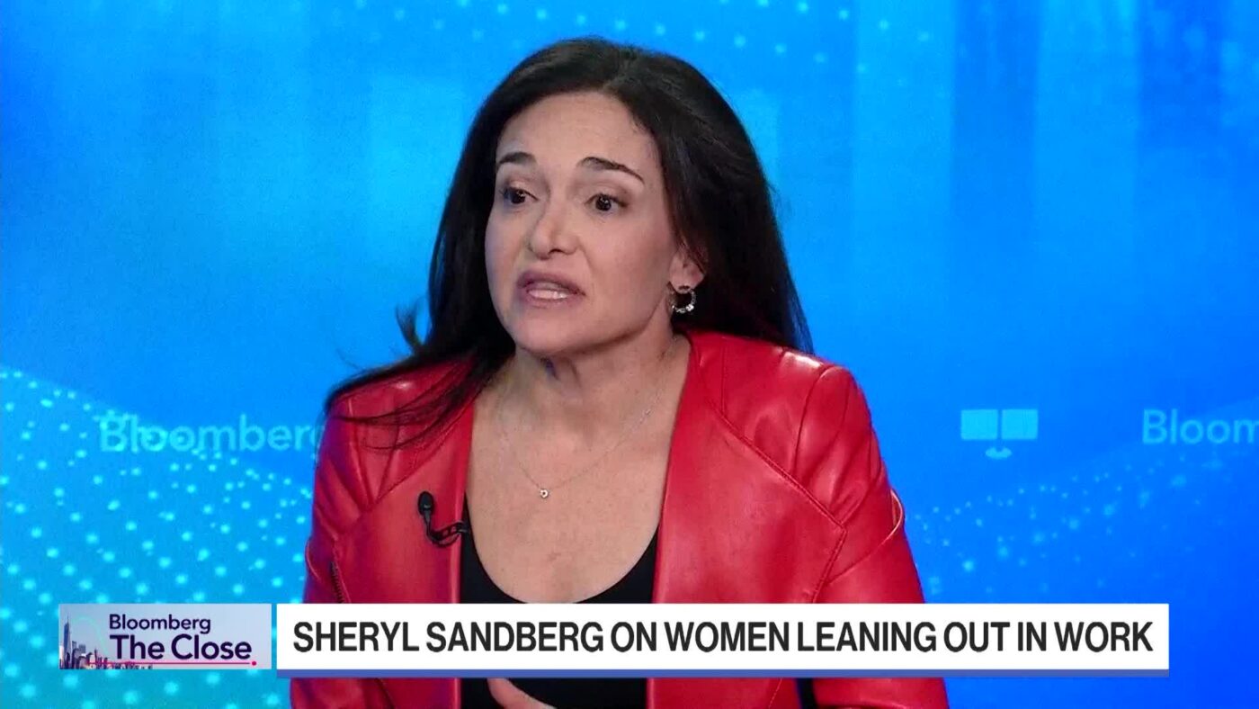 Persona con chaqueta roja en entrevista de Bloomberg, fondo con titular sobre mujeres en el trabajo.