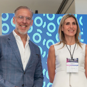 Equipo de Quienes Somos sonriendo: hombre con traje azul, mujer con vestido blanco. Fondo azul con diseño circular. Presentación del equipo.