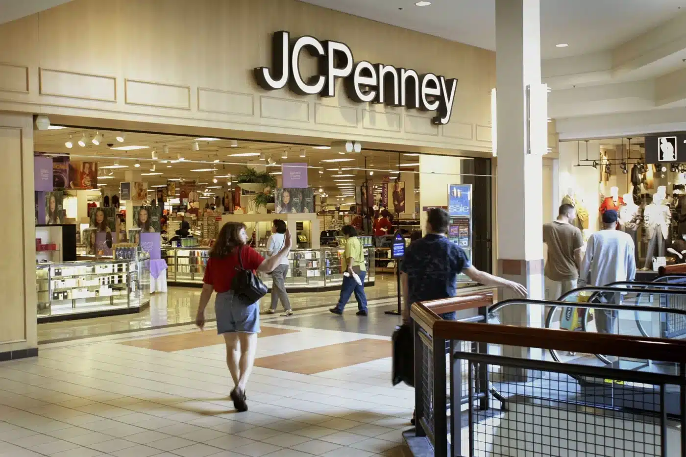Personas pasan y entran a tienda JCPenney en centro comercial, se ven anuncios de renta y exhibidores de ropa dentro.