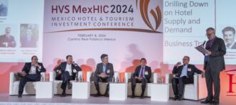 Seis personas con traje sentadas en escenario de panel en HVS MexHIC 2024 conferencia hotelera en México.