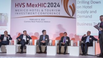 Seis personas con traje sentadas en escenario de panel en HVS MexHIC 2024 conferencia hotelera en México.