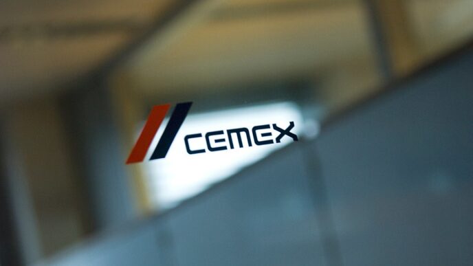 Persona frente a logotipo de Cemex con franjas rojas y azules sobre panel de vidrio en oficina.