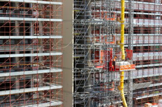 Personas trabajando en plataforma suspendida, rodeadas de andamios y equipo en obra de edificio alto.