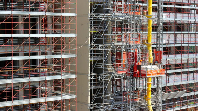 Personas trabajando en plataforma suspendida, rodeadas de andamios y equipo en obra de edificio alto.