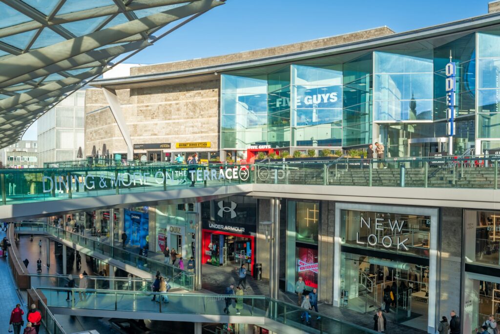 Centro comercial con tiendas de cristales y personas caminando en terraza exterior. Ejemplo del concepto de centro de vida.