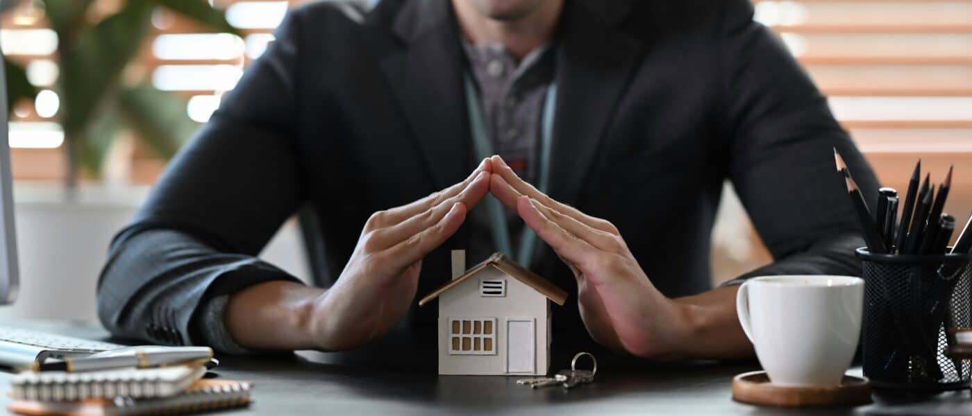 Persona con atuendo formal cubre una maqueta de casa sobre escritorio en Miami.