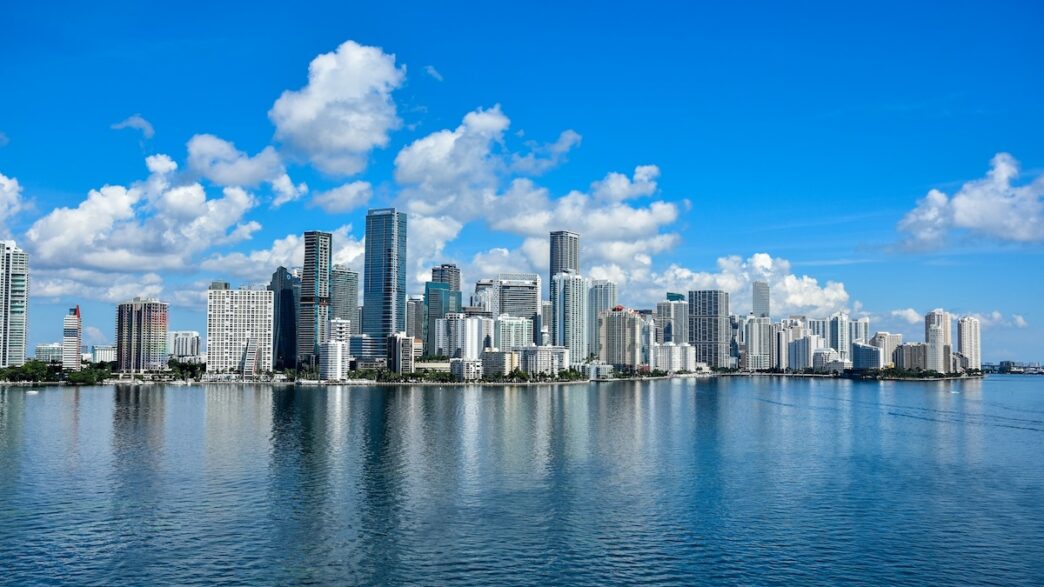 Persona observa skyline de ciudad con edificios altos reflejados en agua tranquila en Florida.