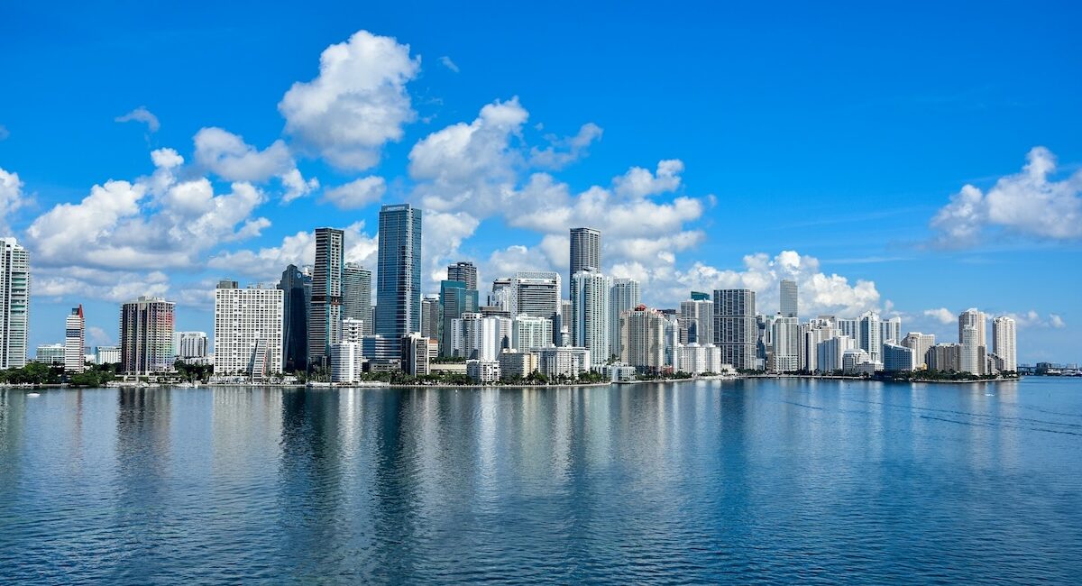 Persona observa skyline de ciudad con edificios altos reflejados en agua tranquila en Florida.
