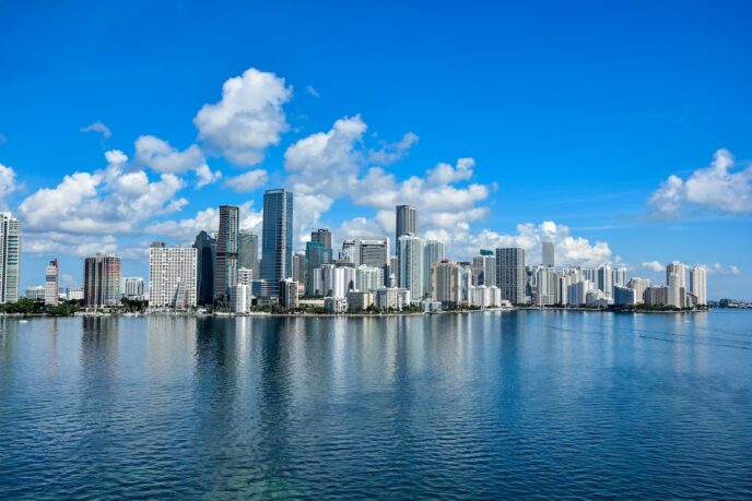 Persona observa skyline de ciudad con edificios altos reflejados en agua tranquila en Florida.