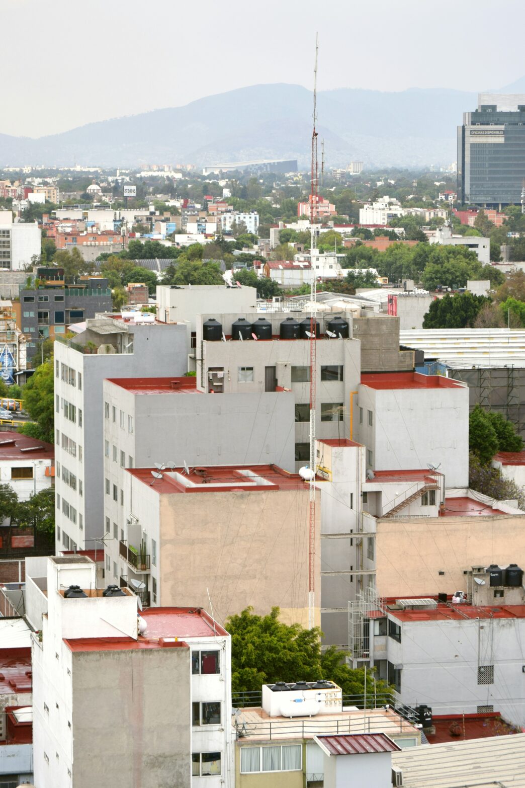 Panorama urbano con edificios de techos blancos y rojos, montañas al fondo y cielo nublado.