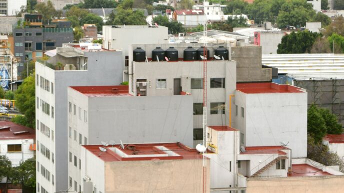 Panorama urbano con edificios de techos blancos y rojos, montañas al fondo y cielo nublado.