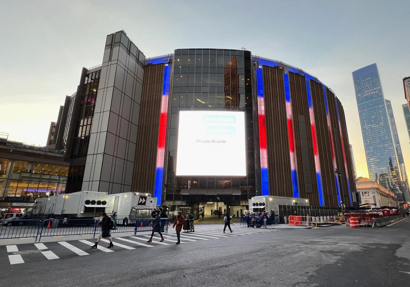 Arena illuminada en rojo, blanco y azul cerca de Penn Station 2026, personas cruzando frente al edificio.