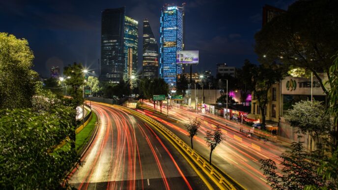 Ciudad de noche con rascacielos iluminados y estelas de luz de vehículos en calle curva.