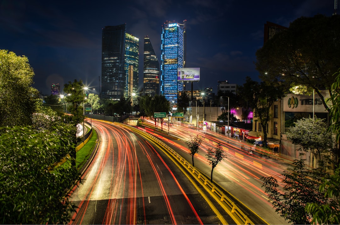 Ciudad de noche con rascacielos iluminados y estelas de luz de vehículos en calle curva.