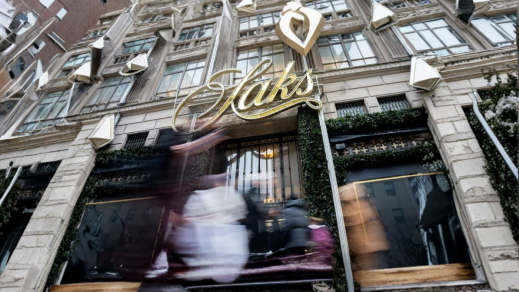 Fachada de Saks con personas difuminadas y anuncio visible de bonos de Saks a 1 centavo en la entrada.