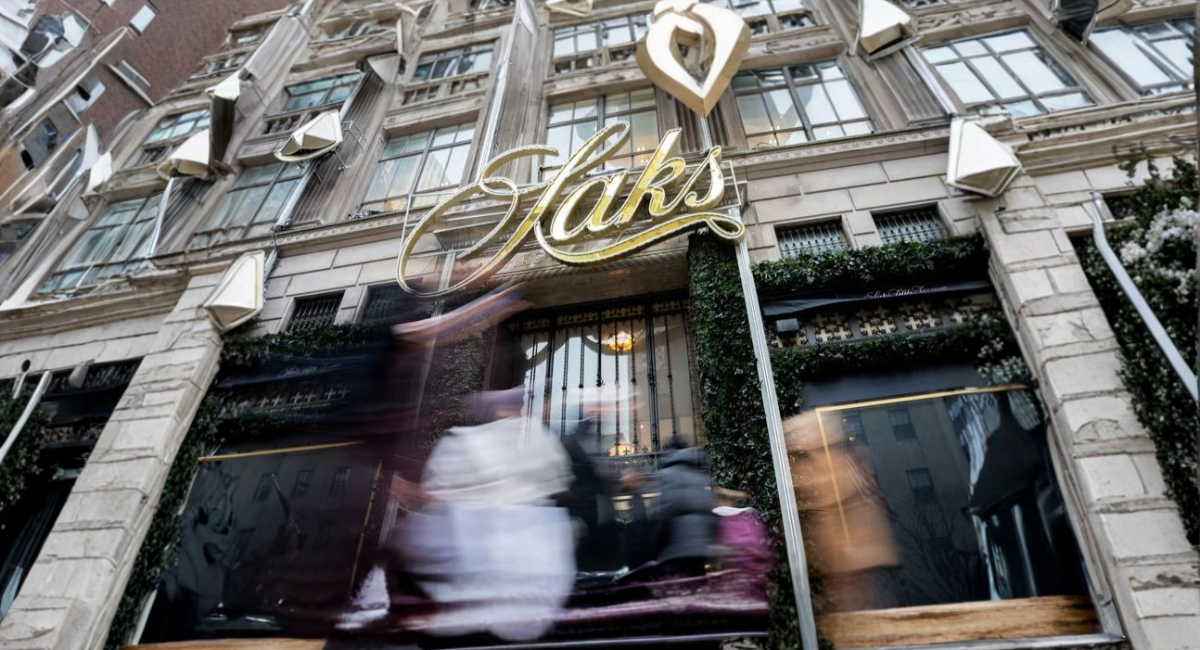 Fachada de Saks con personas difuminadas y anuncio visible de bonos de Saks a 1 centavo en la entrada.