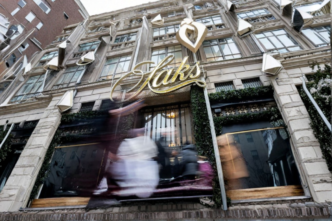 Fachada de Saks con personas difuminadas y anuncio visible de bonos de Saks a 1 centavo en la entrada.
