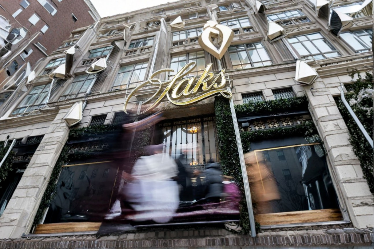 Fachada de Saks con personas difuminadas y anuncio visible de bonos de Saks a 1 centavo en la entrada.