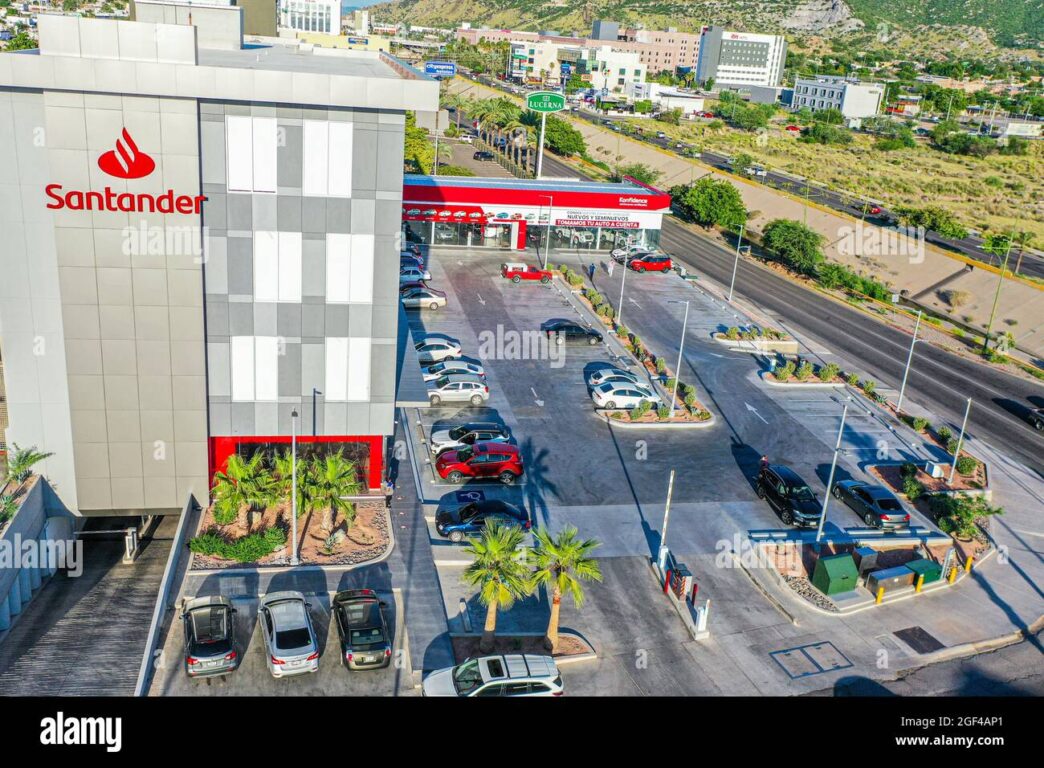 Vista aérea de Santander Distrito Querétaro con estacionamiento, autos y personas junto a avenida concurrida.