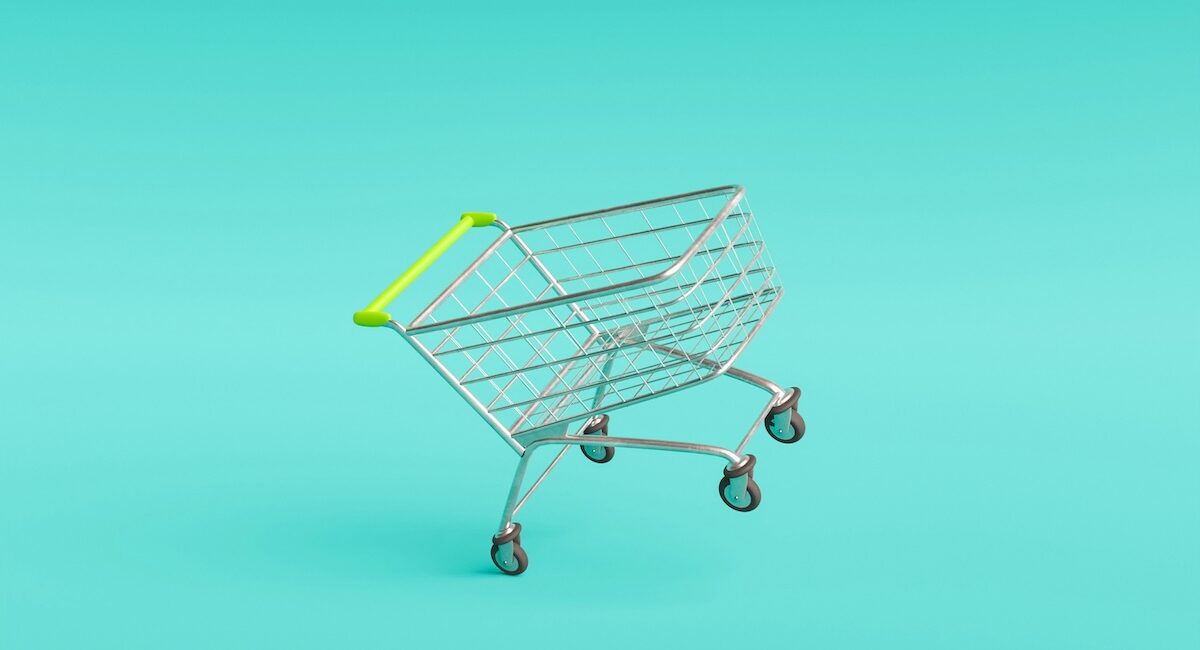 Carrito de metal con asa amarilla vacío sobre fondo turquesa con texto tendencias de retail innovation.