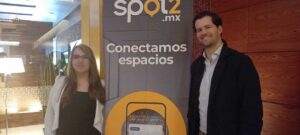 Dos personas junto a lona de Spot2.mx con texto Conectamos espacios en oficinas corporativas Santa Fe.