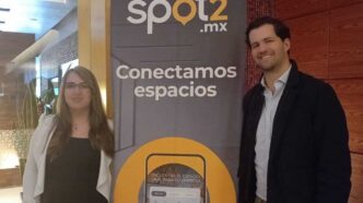Dos personas junto a lona de Spot2.mx con texto Conectamos espacios en oficinas corporativas Santa Fe.