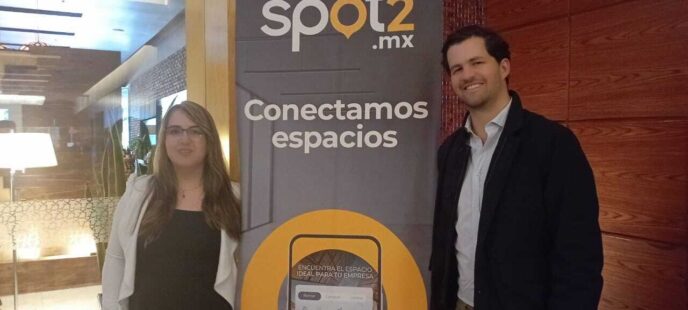 Dos personas junto a lona de Spot2.mx con texto Conectamos espacios en oficinas corporativas Santa Fe.