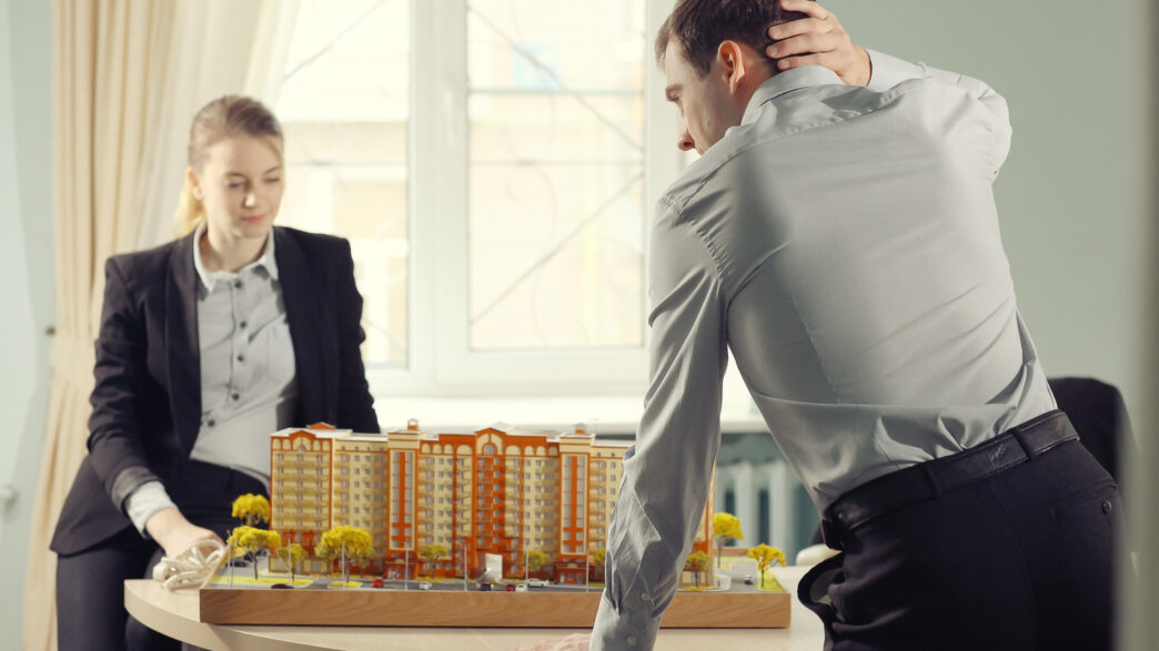 Dos personas con ropa formal observan una maqueta inmobiliaria en México.